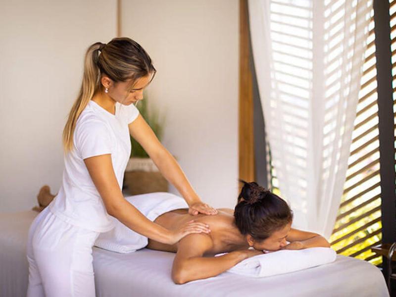 Mujer recibe masaje en una camilla en una habitación luminosa con cortinas.