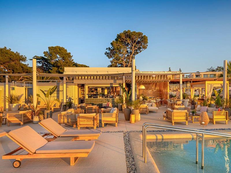 Terraza de hotel con tumbonas y piscina al atardecer bajo un cielo azul.
