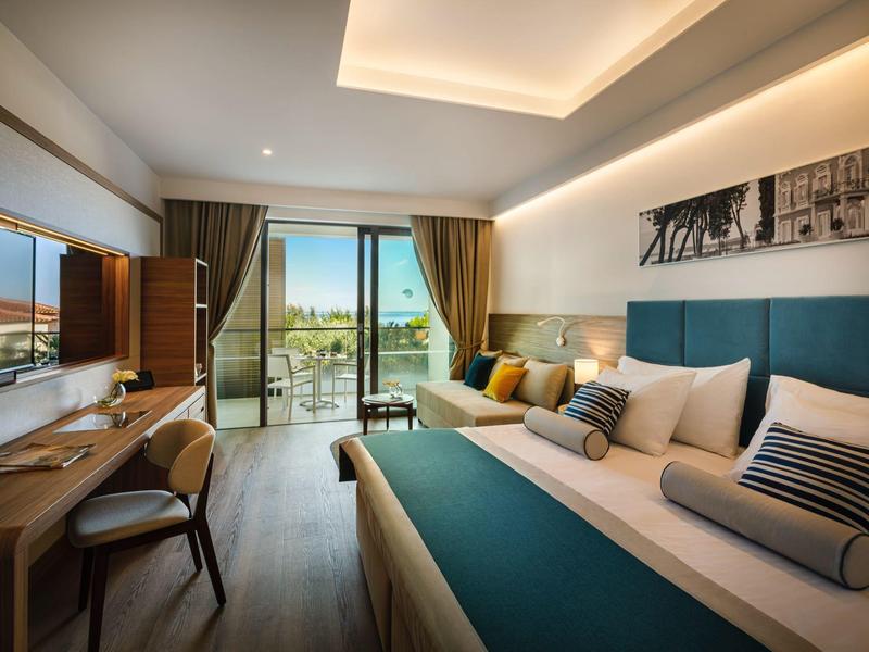 Habitación moderna con cama grande, escritorio, sillón y balcón con vista al aire libre.