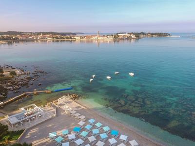 Czyste morze z małymi łodziami i klubem plażowym z niebieskimi parasolami na pierwszym planie.