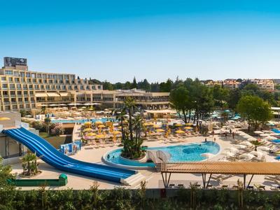 Complexe hôtelier avec piscine, toboggans bleus et terrasses avec chaises longues sous le soleil.