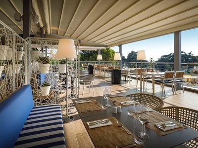 Terrasse de restaurant avec mobilier moderne et vue sur la ville en arrière-plan.