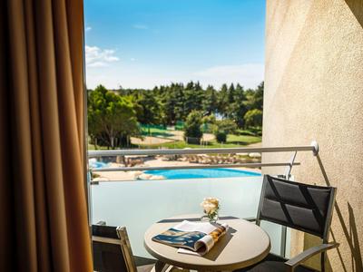 Balcon avec table ronde et chaise surplombant une piscine et des arbres en arrière-plan.
