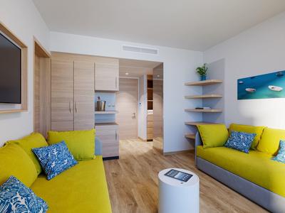 Salon lumineux avec canapés jaunes, coussins bleus et sol en bois clair.