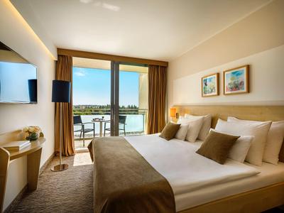 Chambre d'hôtel moderne avec lit double, balcon et vue sur l'eau et les bâtiments.