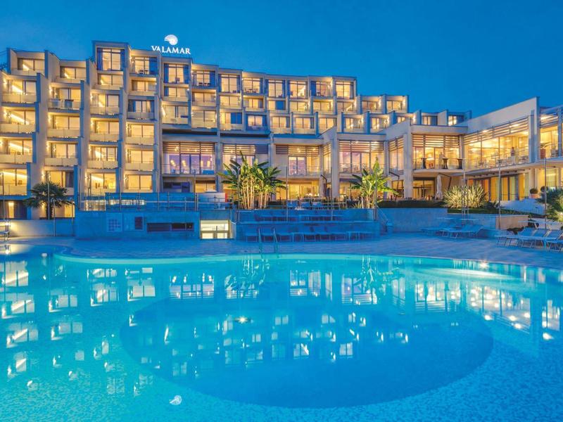 Hôtel moderne avec piscine éclairée la nuit et ciel bleu clair.