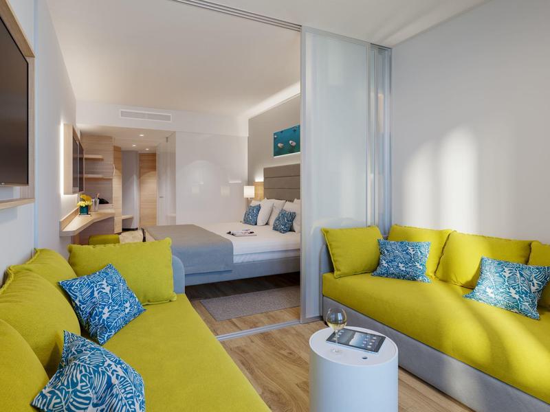 Salon moderne avec canapés jaunes et chambre visible en arrière-plan.