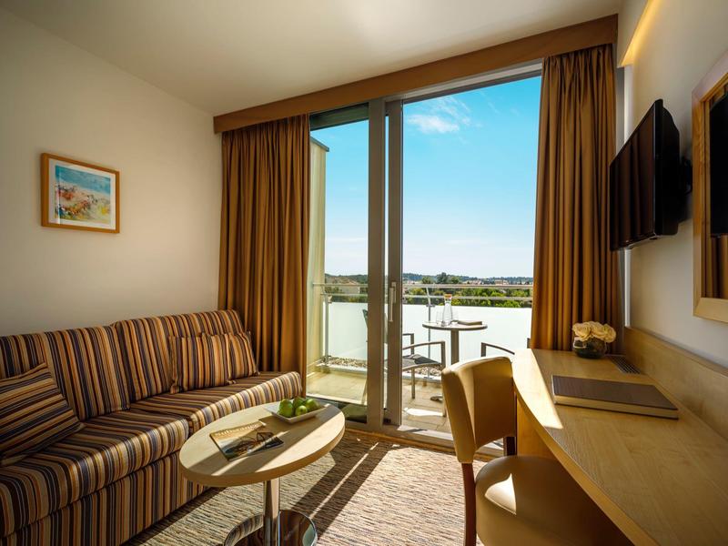 Coin de chambre d'hôtel confortable avec canapé, bureau et vue sur balcon.