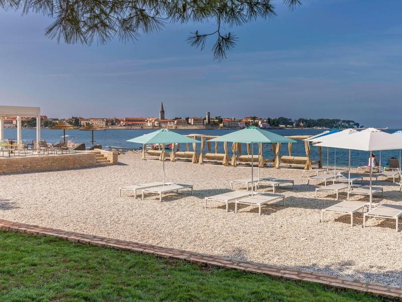 Plage de sable avec parasols et transats face à la mer, sous un ciel clair.