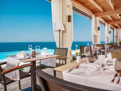 Offenes Restaurant mit gedeckten Tischen und Meerblick, helle Holzdecke und blauer Himmel.