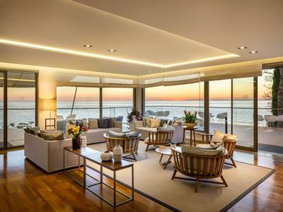 Modernes Wohnzimmer mit großen Fenstern und Blick auf das Meer bei Sonnenuntergang.