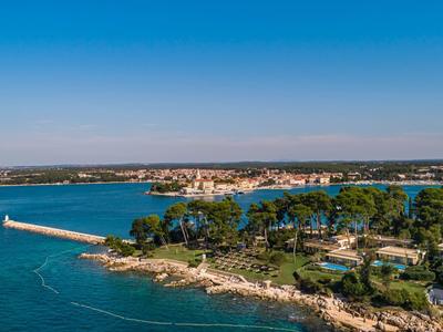 Küstenlandschaft mit grünem Wald, klarem blauem Wasser und einem langen Steg unter blauem Himmel.