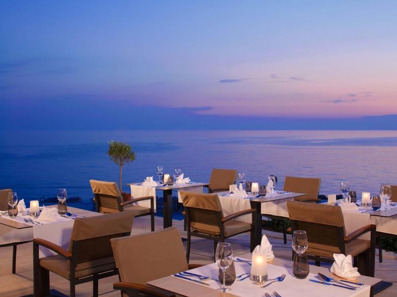 Restaurantterrasse mit gedeckten Tischen, Stühlen und ruhigem Meer im Abendlicht.