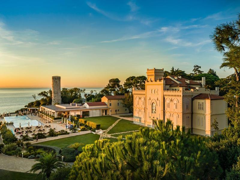 Großes Herrenhaus mit Garten am Meer unter blauem Himmel bei Sonnenuntergang.