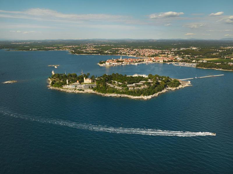 Kleine Insel mit grünen Bäumen und Gebäuden in blauem Meer unter hellem Himmel.