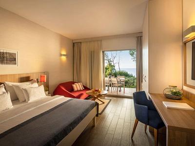 Camera d'hotel moderna con letto matrimoniale, zona salotto e balcone con vista sul verde.