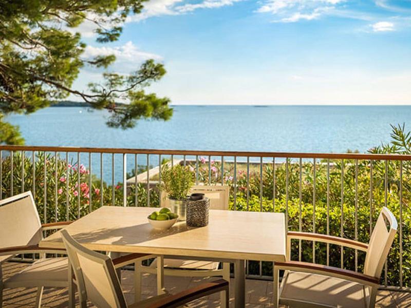 Terrace with a white table, four chairs, and a view of the sea under a partly cloudy sky.