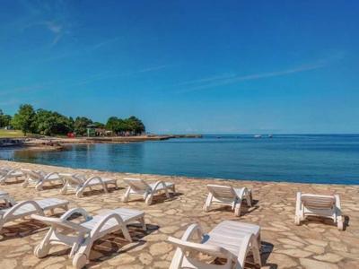 Leerer Sandstrand mit weißen Liegestühlen unter blauem Himmel am ruhigen Meer.