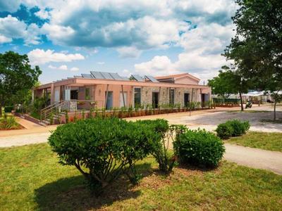 Un edificio de hotel con paredes rosas rodeado de arbustos y un cielo despejado.
