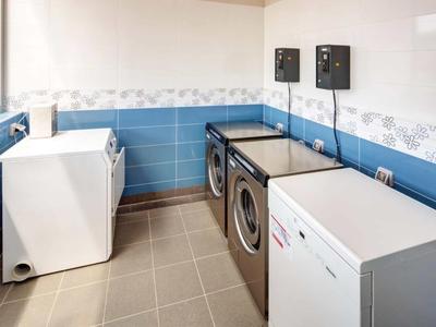 Cuarto de lavandería limpio con dos lavadoras de carga frontal, secadora y paredes con azulejos claros.