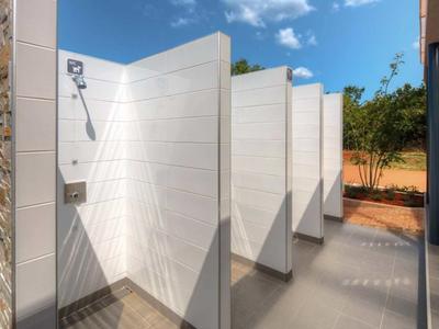 Área de ducha al aire libre con varias divisiones blancas y cielo azul.
