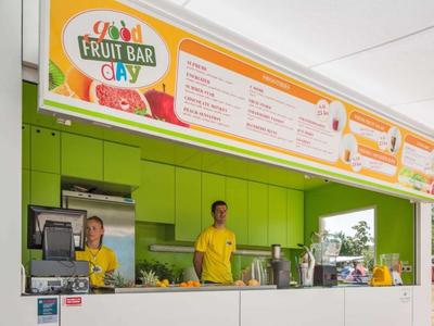 Puesto moderno y colorido de bar de frutas con dos empleados en camisetas amarillas y menú arriba.