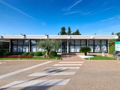 Edificio de hotel bajo con grandes ventanales, plantas verdes y cielo azul de fondo.