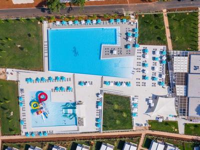 Luftaufnahme eines Hotelpools mit Liegestühlen und umgebenden Grünflächen