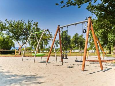 Parque infantil con columpios y estructura de escalada en un parque soleado con árboles.