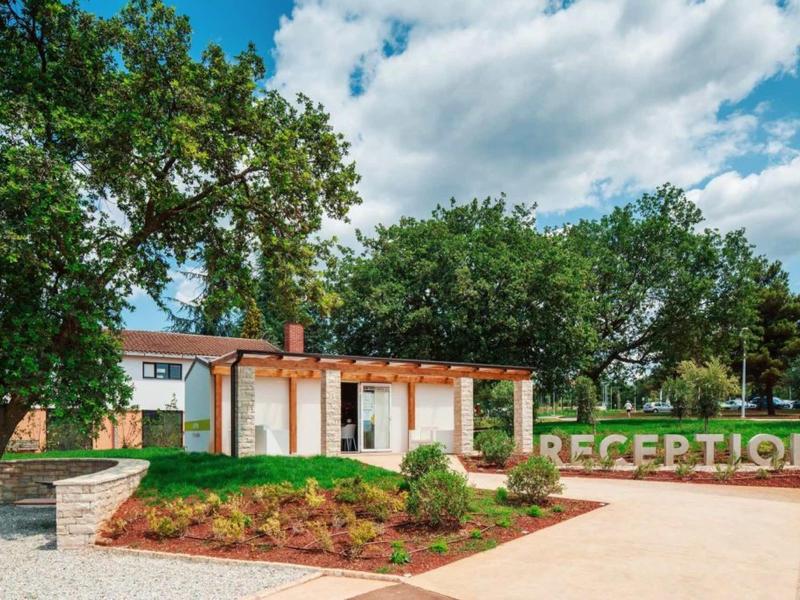 Área de recepción moderna con pérgola y rodeada de árboles bajo un cielo azul.