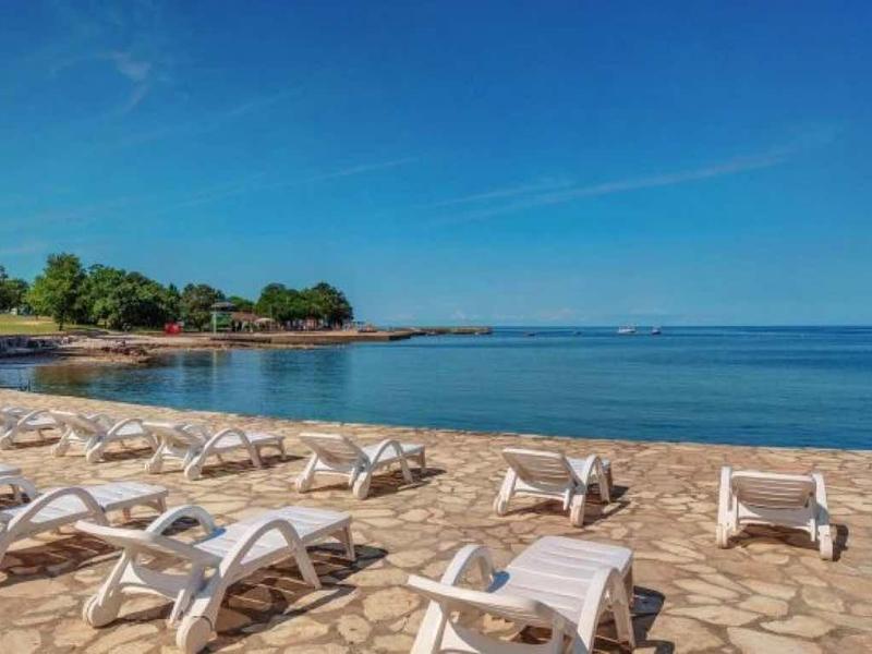 Playa de arena vacía con tumbonas blancas bajo cielo azul junto al mar tranquilo.