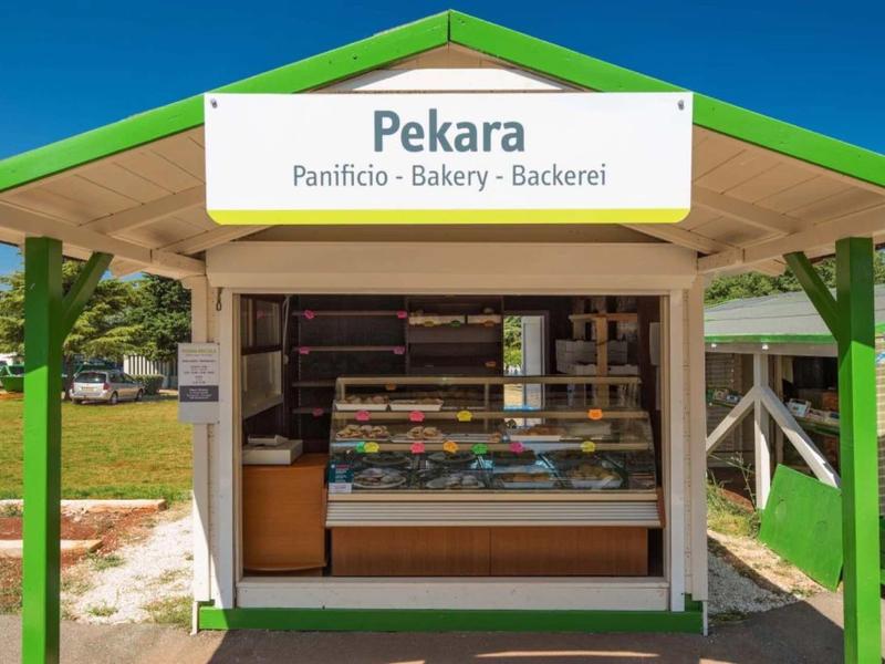 Pequeña panadería al aire libre con toldo verde y estanterías de pan visibles