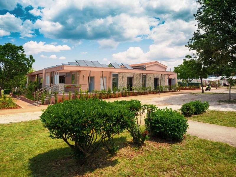 Un edificio de hotel con paredes rosas rodeado de arbustos y un cielo despejado.