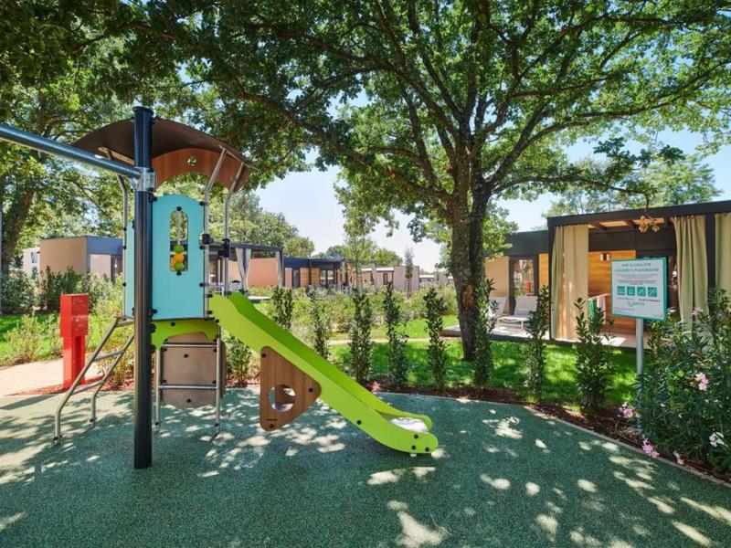 Parque infantil con tobogán y árboles en el jardín de un hotel en un día soleado.