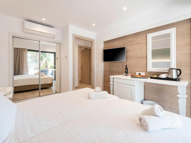 Habitación de hotel moderna con cama doble, televisor de pantalla plana y minibar bajo un espejo.