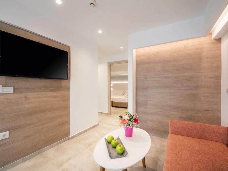 Habitación moderna de hotel con televisor en la pared, sofá rojo y una mesa pequeña con frutas y flores.