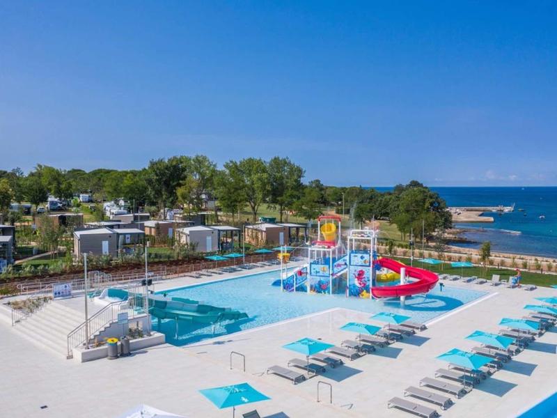 Gran piscina exterior con toboganes de agua y tumbonas junto al mar bajo cielo despejado.