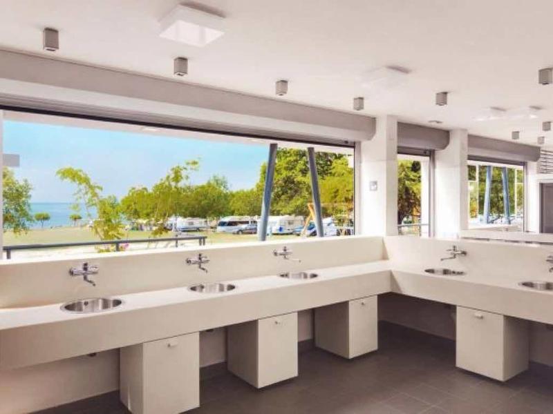 Área de lavado moderna y luminosa con varios lavabos y grandes ventanas con vista al mar.