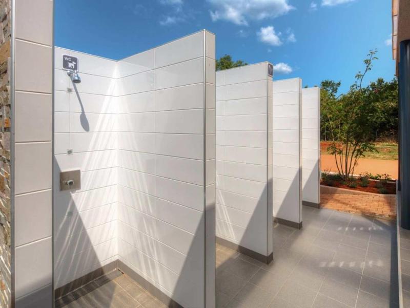 Área de ducha al aire libre con varias divisiones blancas y cielo azul.