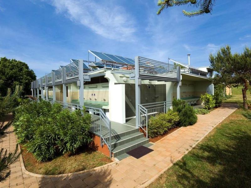Casa de vacaciones moderna con terraza y protección solar bajo un cielo azul en un entorno verde