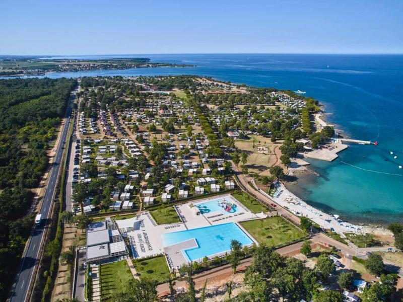 Vista aérea de un resort costero con piscinas, área de acampada y mar azul en un día soleado.