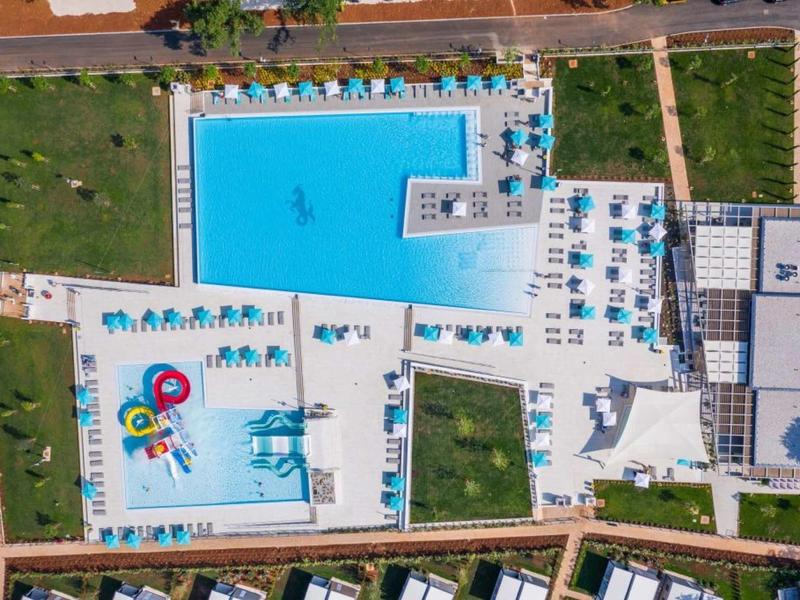 Vista aérea de un hotel con grandes piscinas, tumbonas y áreas verdes en un resort.