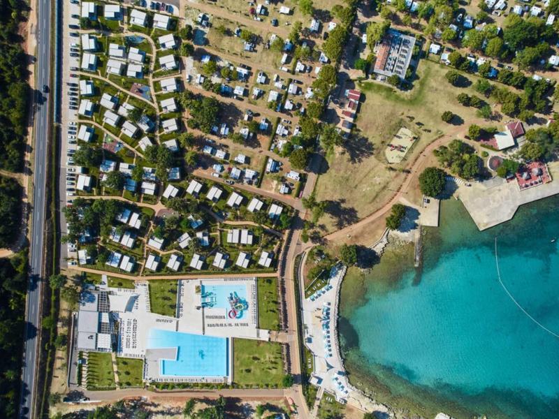 Vista aérea de un resort con piscinas cerca de un mar azul claro y áreas para autocaravanas.