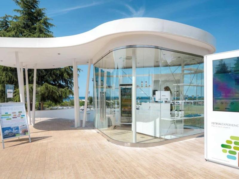 Edificio de recepción hotelera moderna, redonda con paredes de vidrio y techo blanco bajo un cielo azul.