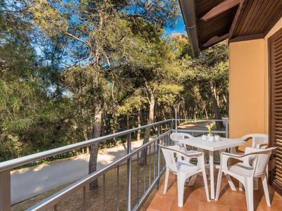 Balcony with table and four white chairs overlooking trees and blue sky.