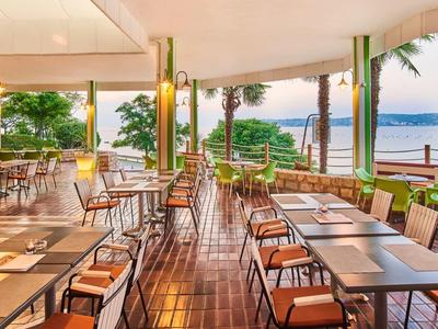 Open restaurant terrace with wooden floor and sea view at sunset.