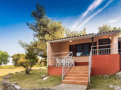 Haus mit rotem Sockel, verglaster Veranda, umgeben von Bäumen und grünem Gras unter blauem Himmel.