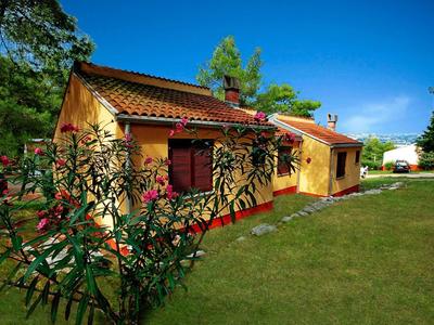 Yellow single-family house with red shutters and green lawn on a sunny day