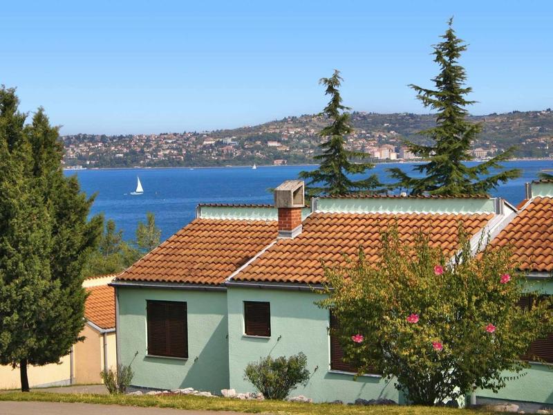 Dom z czerwonym dachem przy jeziorze z żaglówkami na pagórkowatym terenie.