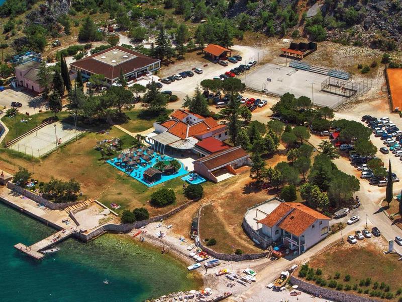 Kompleks hotelowy z basenem, parkingiem i bezpośrednim dostępem do wody na zielonym terenie.